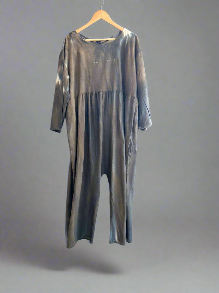 Gray jumpsuit on a hanger against a white brick wall.