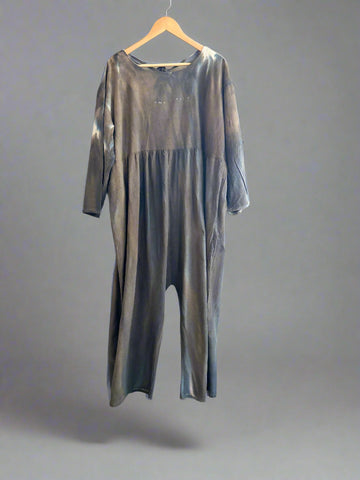 Gray jumpsuit on a hanger against a white brick wall.